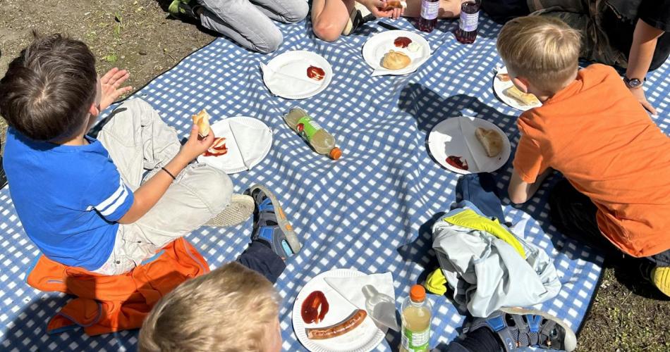 Kinder beim Würstkessen auf Picknickdecke 
